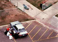 Students hide behind a cop car as the officer exchanges fire with the shooters.